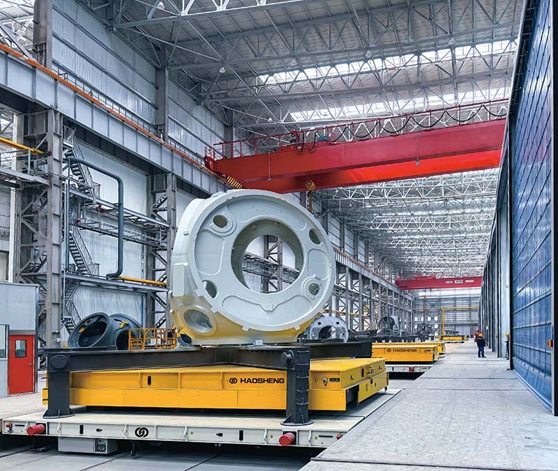 Heavy-duty yellow transfer vehicles carrying large industrial components in a manufacturing hall 