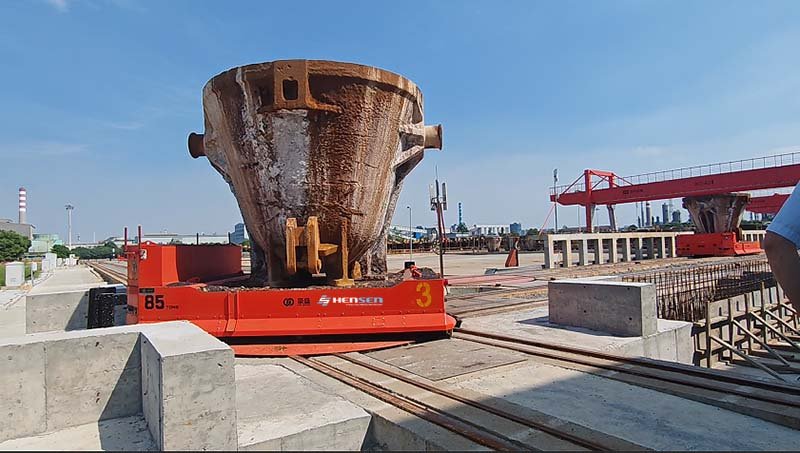 85-ton orange rail guided transfer vehicle carrying a large industrial vessel ladle at a rail intersection